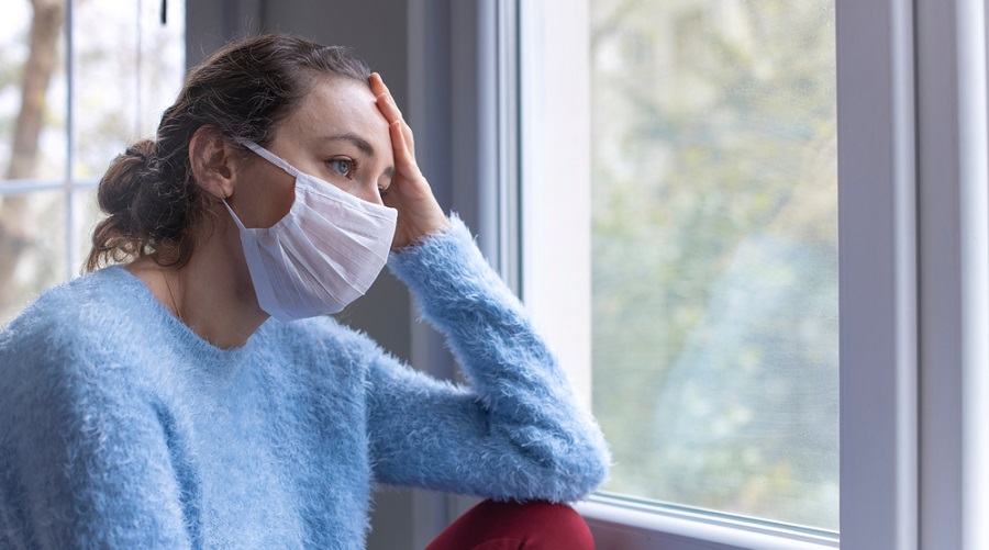 Worried woman with face mask looking out of window