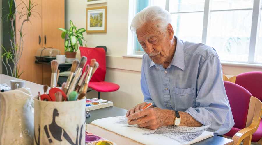 An older man focused on drawing an image of a landscape
