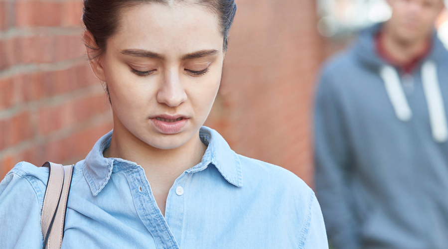 A young woman looks distressed while a young man looks at her behind her back