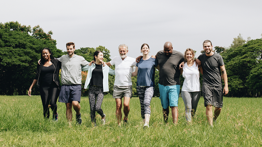 A group of smiling people walking across a field with arms around each others' shoulders