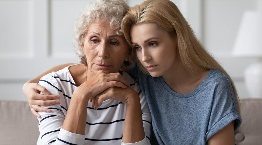 An older and younger woman embrace while looking sad