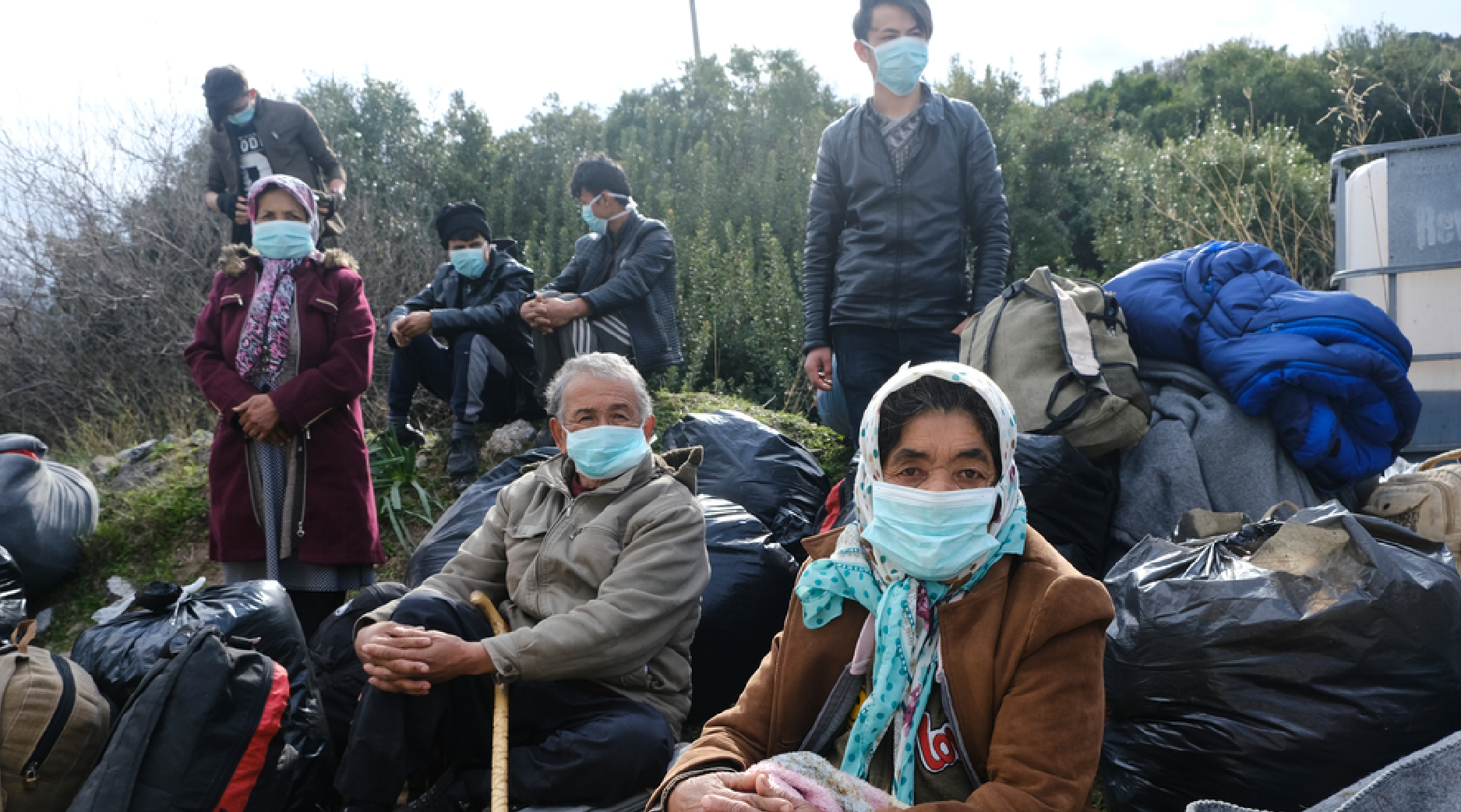 A group of migrants sitting on the ground with bags